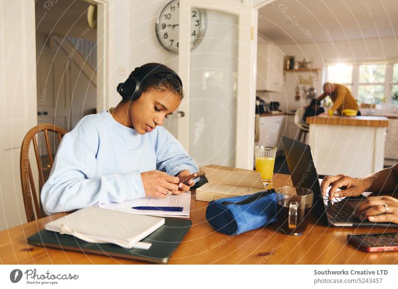Teenager-Mädchen macht Hausaufgaben, trägt Kopfhörer und benutzt ein Telefon lernen Zelle Handys Mobile zuhören Konzentration Notebook anhaben Buch Lernen