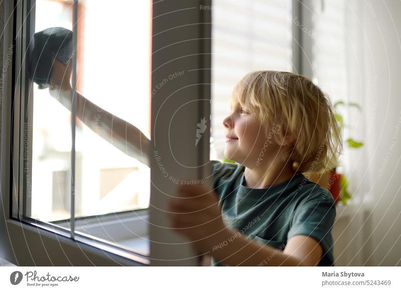 Niedlicher kleiner Junge, der zu Hause ein Fenster putzt. Kind hilft Eltern  bei der Hausarbeit, zum Beispiel beim Fensterputzen in seinem Haus. Kinder  bei der Hausarbeit. - ein lizenzfreies Stock Foto von