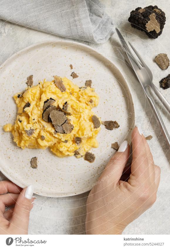 Hände mit Teller mit Rührei mit frischen schwarzen Trüffeln Draufsicht, Gourmet-Frühstück verschlüsselt Eier aufgeschnitten Italien Gabel Messer Italienisch
