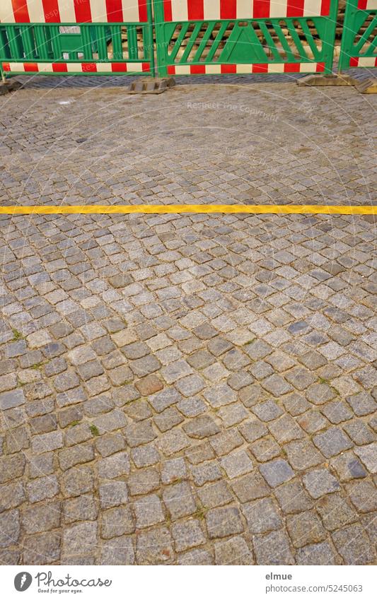 grüne Plastik Warnbaken mit rot-weißen Streifen und eine gelbe Linie auf einer Kopfsteinpflaster Straße / Straßenbaumaßnahme Einschränkung Baustelle Fahrbahn