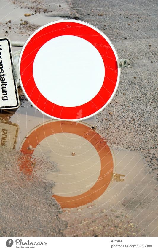 Verkehrszeichen "Durchfahrverbot" mit Zusatzzeichen "Veranstaltung" liegen auf dem Asphaltboden und spiegeln sich in einer Pfütze verkehrsberuhigte Zone