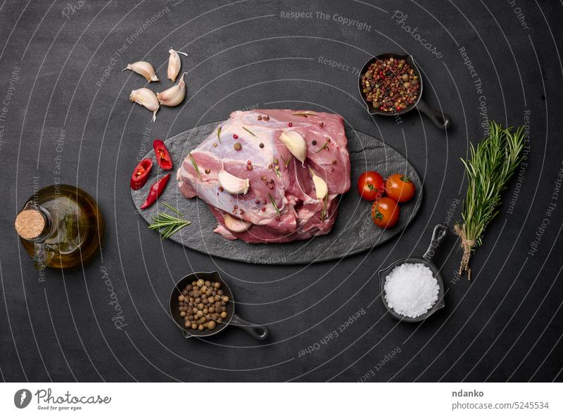 Ein Stück Schweineschinken auf einem schwarzen Brett und Gewürze Olivenöl, Salz, Rosmarin Zweig und Pfeffer Knoblauch Lebensmittel Spielfigur Scheibe