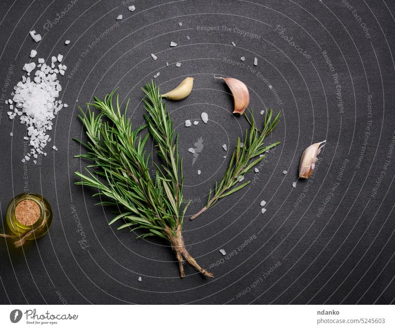 Grobes weißes Salz, Pfefferkörner und Rosmarinzweige auf einem schwarzen Tisch verstreut, Zutaten für die Zubereitung von Fisch und Fleisch Knoblauch