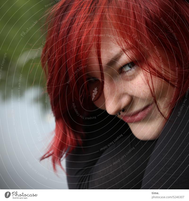 lächelnde Frau am See Blick rothaarig weiblich verschmitzt Natur feminin Blick in die Kamera Gesicht langhaarig Halbprofil