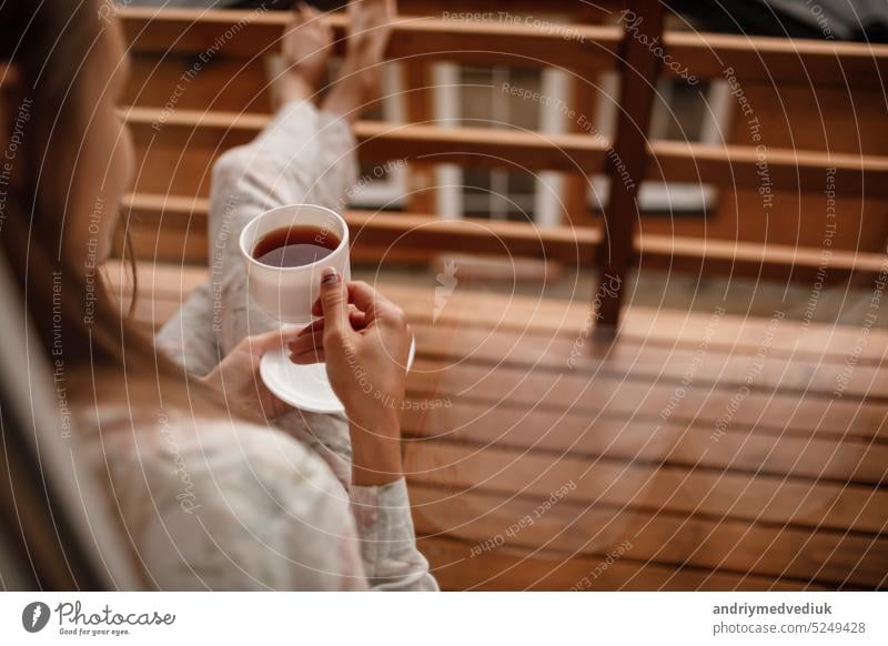 Junge Frau stehend nach dem Duschen am Morgen auf dem Balkon des Hotels. hält eine Tasse Kaffee oder Tee in ihren Händen. Blick nach draußen Natur Wald und Berg