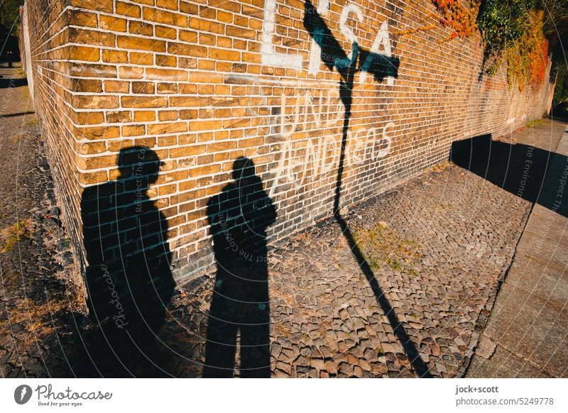 Lisa und Andreas stehen an der alten Friedhofsmauer Mauer Straßenkunst Kreuzberg Berlin Kreativität Spray Wort Sonnenlicht Kontrast Silhouette Schattenspiel