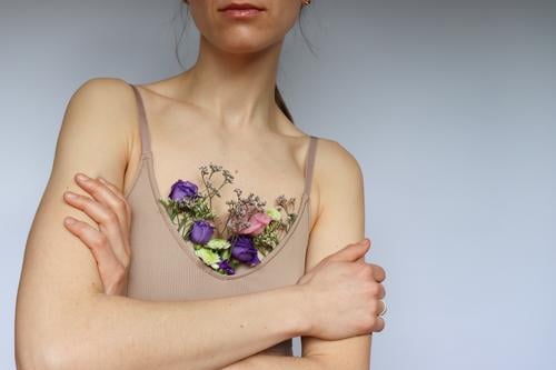 Eine Junge Frau mit gekreuzten Armen und in einem beigen Brusthalter in dem bunte Blumen stecken. gekreuzte Arme Blumen im Brusthalter beider Brusthalter Bra
