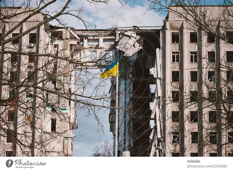 Flagge der Ukraine vor dem Hintergrund eines zerstörten Gebäudes in der Ukraine. Das Gebäude wurde durch eine russische Fliegerbombe zerstört Fahne Haus