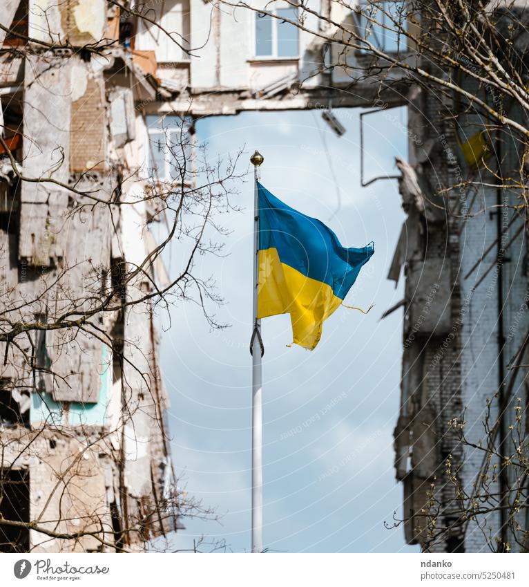 Flagge der Ukraine vor dem Hintergrund eines zerstörten Gebäudes in der Ukraine Fahne gelb blau unerschütterlich stark ununterbrochen ramponiert