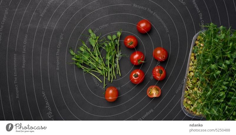 Rote Tomate und gekeimte Erbsensamen auf schwarzem Hintergrund, Mikrogrün für Salat, Detox. Ansicht von oben roh rot Wurzel Salatbeilage Paprika Pflanze Samen