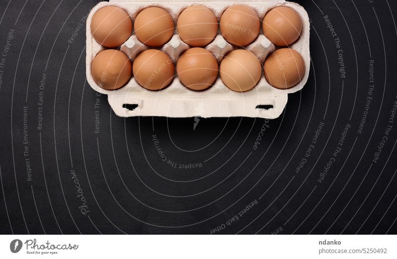 Rohe braune Hühnereier in einem Papierkartonbehälter auf schwarzem Hintergrund, Ansicht von oben Ei Eierschale roh Panzer zehn Kasten Frühstück ungekocht