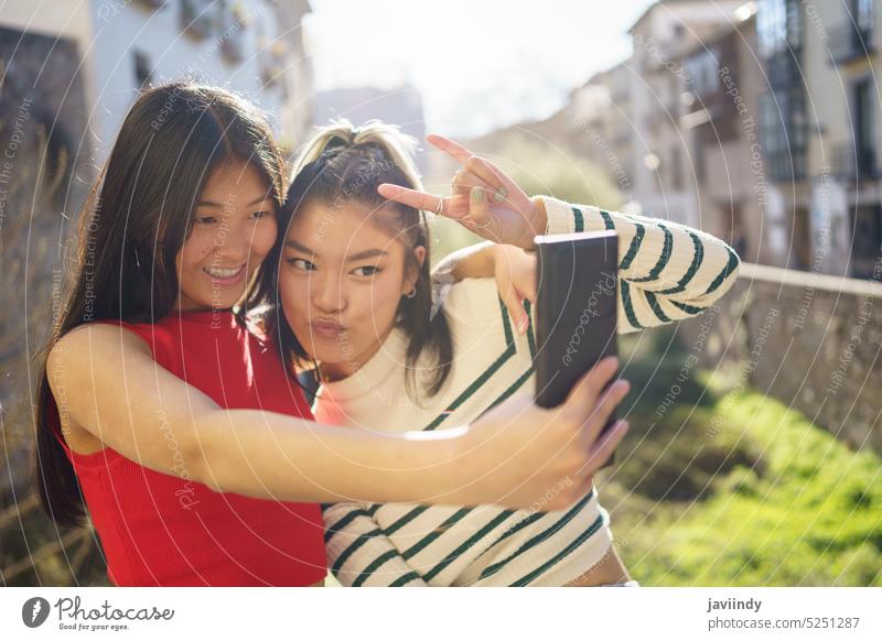Lächelnde asiatische Freundinnen nehmen Selfie auf der Straße Frauen Smartphone Zusammensein schießen heiter fotografieren Glück gestikulieren Felsen benutzend