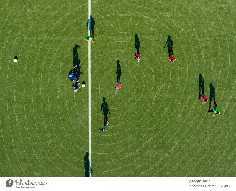 Fußballspieler im Training mit mehreren Bällen auf einem Spielfeld mit Kunstrasen. Blick streng von oben. Die Mittellinie ist zu sehen. Spieler Rasen