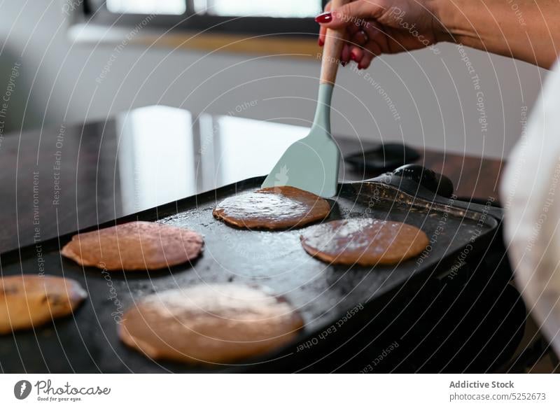 Anonyme erwachsene Hausfrau beim Backen von Pfannkuchen auf der Grillplatte Frau Koch Frühstück Bratpfanne Flip Vorrichtung eingießen Teig braten Spachtel