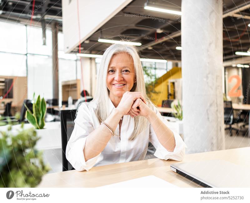 Fröhliche ältere Mitarbeiterin sitzt am Tisch im Büro Frau Laptop bei der Arbeit modern Business Arbeitsbereich Job Unternehmen Geschäftsfrau positiv Lächeln