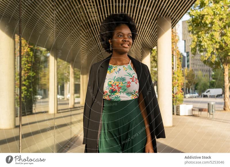 Stilvolle ethnische Frau in der Nähe eines Gebäudes stehend besinnlich verträumt nachdenklich urban Großstadt Sonne Afroamerikaner Straße Windstille jung