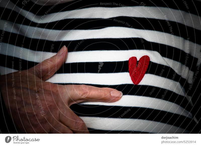 Ein aufgesticktes rotes Herz auf einen Thirt , mit schwarzen und weißen Streifen und zwei Finger zeigen darauf. herzform Gefühle Romantik Menschenleer Farbfoto