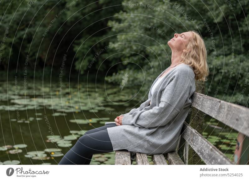 Entspannte Frau sitzt auf einer Bank in der Nähe eines Sees ruhen Lotosblatt Baum sich[Akk] entspannen Landschaft Vergnügen Wasser verträumt nachdenken