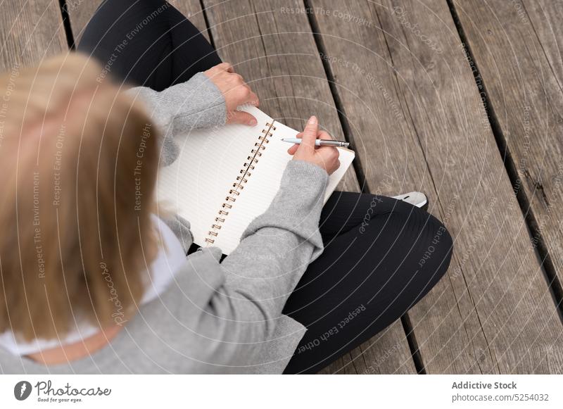 Crop-Frau schreibt Notizen in Notizbuch auf Holzsteg zur Kenntnis nehmen schreiben Information Schönschreibheft Notebook Pier Planer Zeitvertreib lässig sitzen