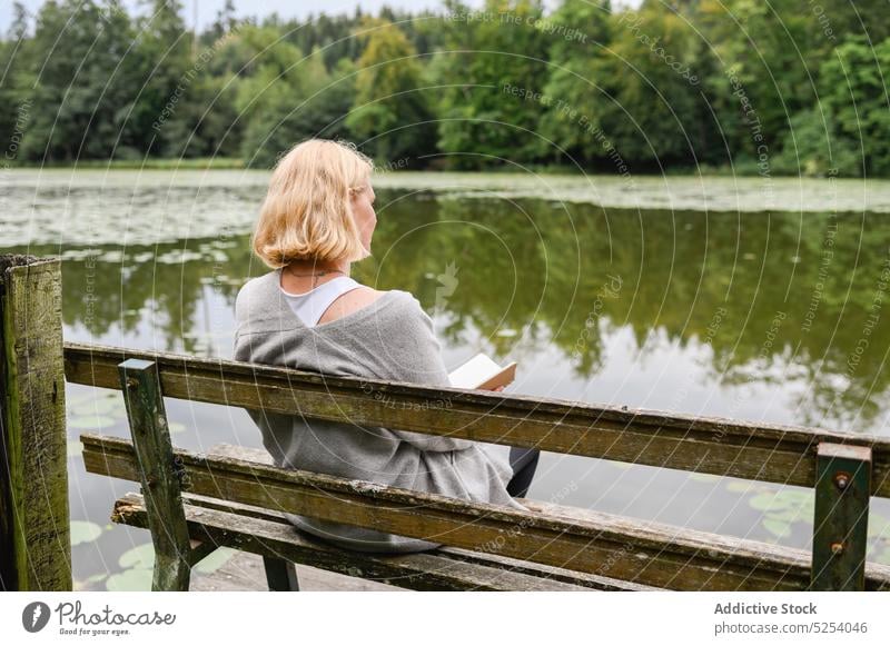 Nachdenkliche Frau mit Notebook auf einer Bank am See sitzend lesen Hinweis Information Buch Schönschreibheft Park Natur Baum nachdenklich Denken Gedanke