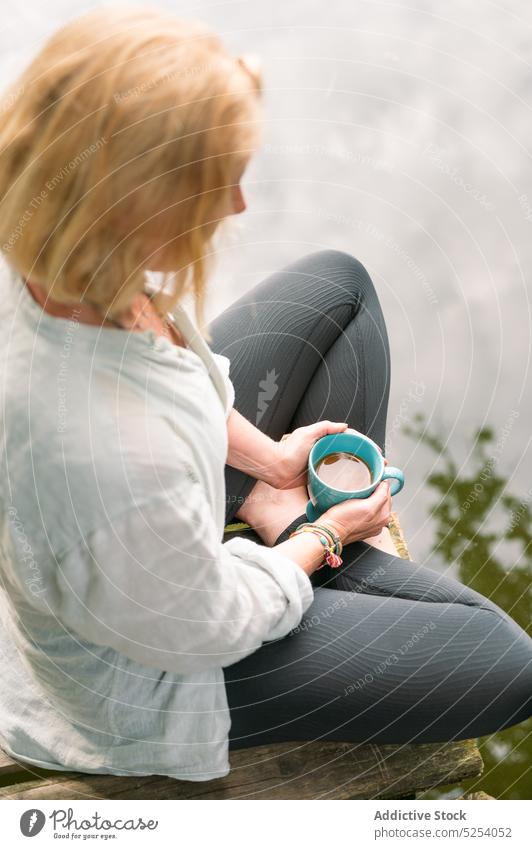 Frau mit Tasse heißem Tee am See sitzend Heißgetränk Erholung Pier Beine gekreuzt Natur aromatisch Harmonie ruhen Landschaft sich[Akk] entspannen Getränk Kaffee
