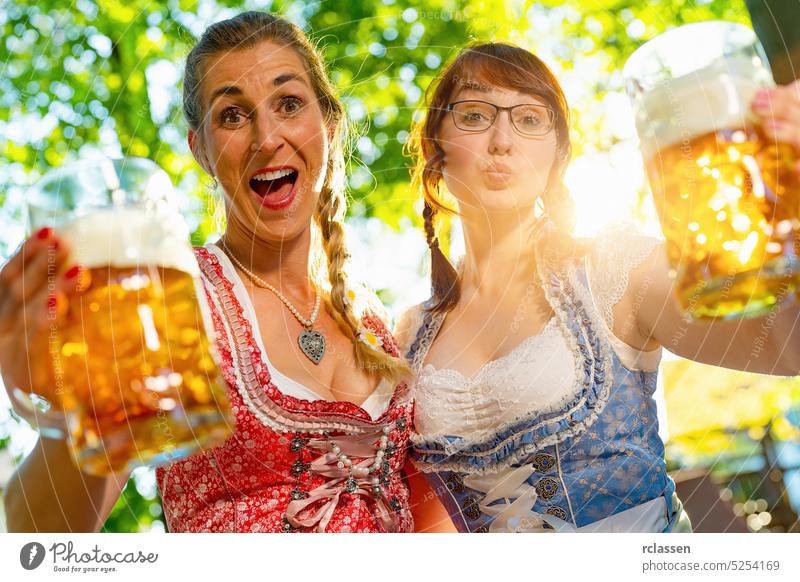 Freundinnen schauen und schreien, küssen sich in die Kamera und sagen Prost oder stoßen mit einem Krug Bier im bayerischen Biergarten oder auf dem Oktoberfest an