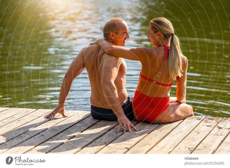 Mutter und Vater genießen den Sommer am Steg eines Sees im Sommer Liebe Umarmung Mann männlich Anlegestelle Schilfrohr Urlaub Badebekleidung Bikini Bayern