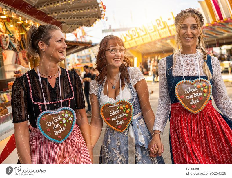 Freundinnen, die sich auf dem bayerischen Jahrmarkt oder dem Oktoberfest im Dirndl mit der Aufschrift "Schenk mir dein Herz, Du bist die beste" am Lebkuchenherz vergnügen