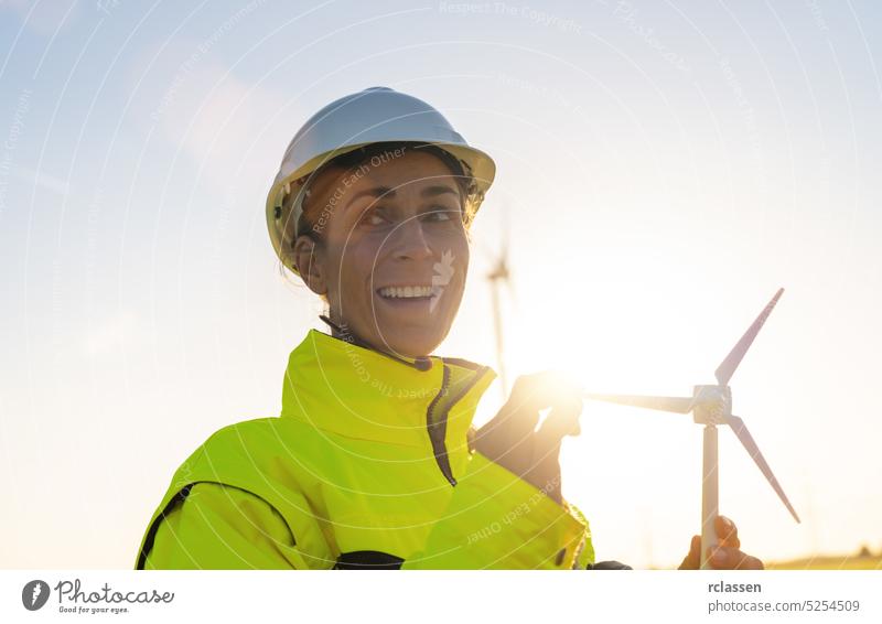 glückliche Ingenieurin, die ein Windturbinenmodell hält und die Windturbinen überprüft. Neue Energie Konzept Bild Sonnenuntergang Sicherheitsweste Schutzhelm
