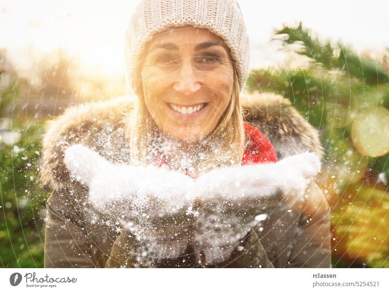 Winter Girl Blowing Snow in frostigen Winter Park und lächelnd. Frau, die Spaß im Winter Zeit an Weihnachten Handschuhe Tanne Weihnachtsbaum Schnee Glück