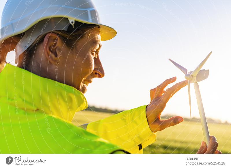 Ingenieurin hält Windradmodell und spielt mit Propellern bei Sonnenuntergang Sicherheitsweste Schutzhelm Frau Bauernhof Turbine Techniker Menschen Business
