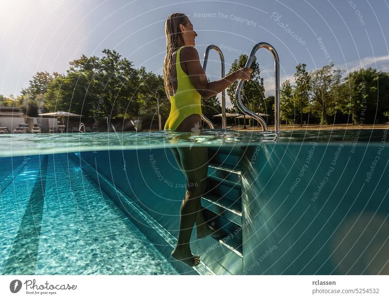 junge Frau steht an einer Leiter in einem Schwimmbad, geteiltes Ober- und Unterwasserfoto Laufmasche Handläufe oben Hälfte Split thermisch Resort platschen