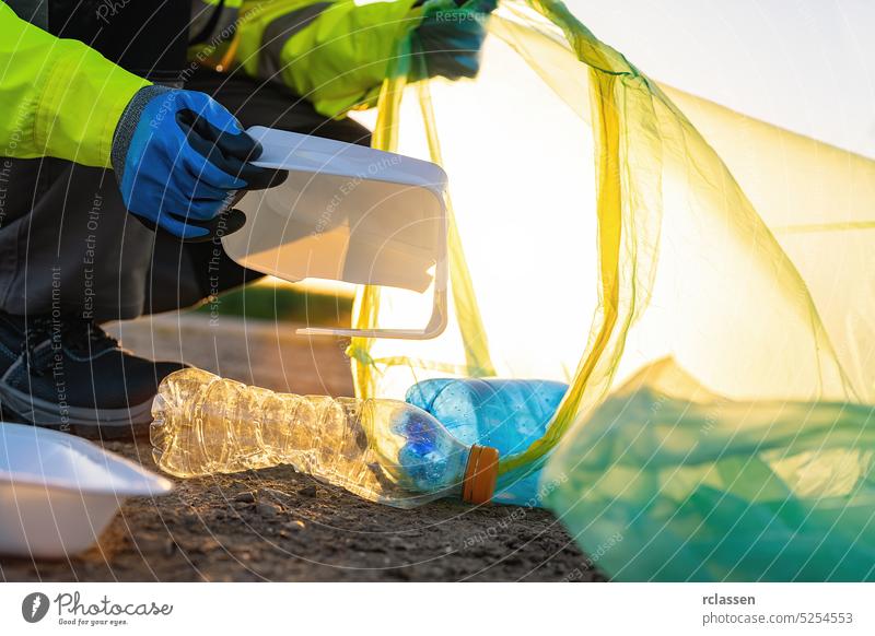 Freiwilliger Mann sammelt Plastikmüll im Park bei Sonnenuntergang. Reinigung der Umwelt Konzept Müll Aktivist Tasche Behälter Flasche Sauberkeit Erhaltung