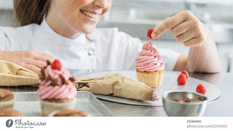 Frauen in der Konditorei arbeiten an Muffins und legen eine Himbeere oben drauf Hand Spritzbeutel rosa Himbeeren Kuchen Cupcake Geburtstag Zucker Party Bonbon
