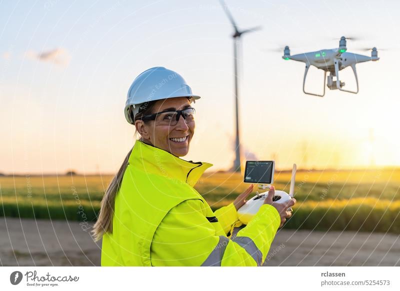 Happy Female Operator inspiziert Windkraftanlage mit Drohne bei Sonnenuntergang. Drohne Inspektion Konzept Bild. erneuerbare Energien Windpark in Europa Lächeln