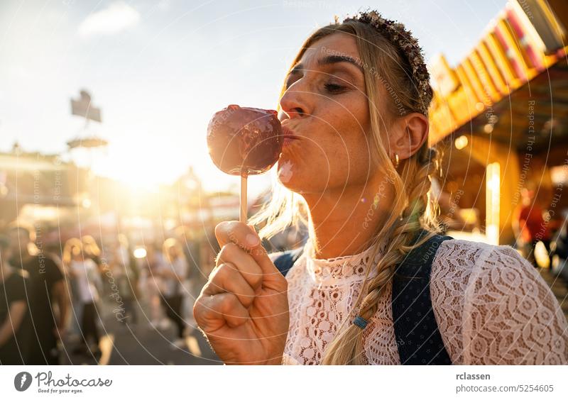 Frau isst kandierten Apfel auf dem Oktoberfest und trägt Dirndl in Deutschland glasierter Apfel süß Zucker rot Party biergarten Freundinnen