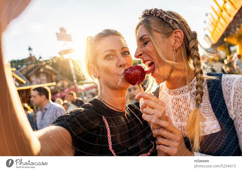 Zwei Freundinnen machen ein Selfie im Dirndl und mit kandierten Äpfeln auf einem bayerischen Volksfest oder Oktoberfest oder in Tracht oder Dirndl Foto
