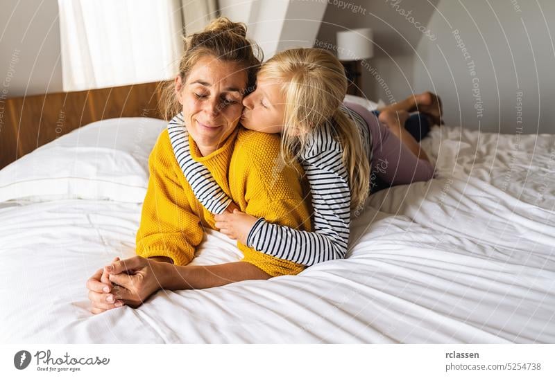 Kleines Mädchen küsst ihre Mutter auf dem Bett liegend und genießen Sie die Zeit zu Hause. Muttertag oder die Liebe der Mutter Konzept Bild Mama Familie