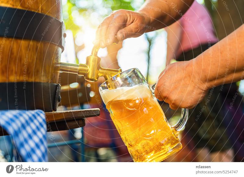 Bayerische Kellnerin in Tracht und Dirndl schenkt im Biergarten ein großes Lagerbier aus dem Holzfass ein. Hintergrund für Oktoberfest, Volks- oder Bierfest (Deutsch für: O'zapft is!)