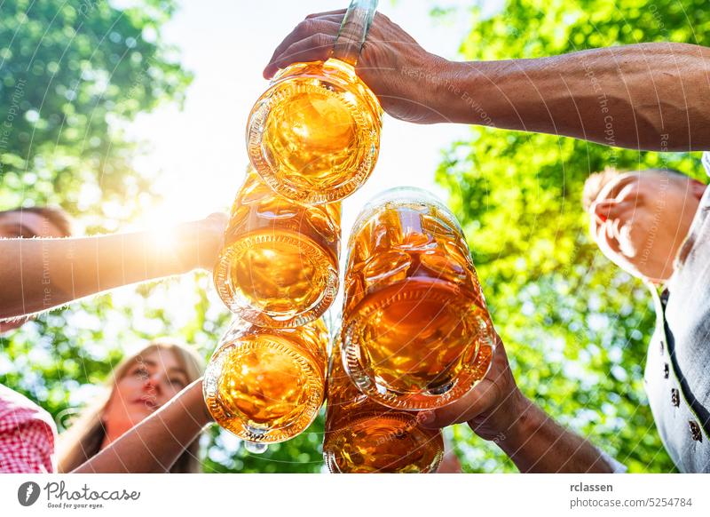 Gruppe fröhlicher bayerischer Freunde, die auf dem Oktoberfest, Volksfest oder Bierfest in Deutschland Bier trinken und darauf anstoßen Wasserhahn Hände brezen