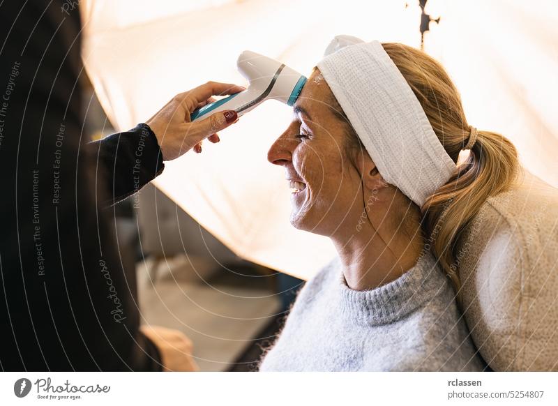 Make-up-Assistentin, die das Gesicht eines Models mit einer elektrischen Bürste für ein Fotoshooting oder einen Film vor Ort reinigt. Gerät Gesichtsbehandlung