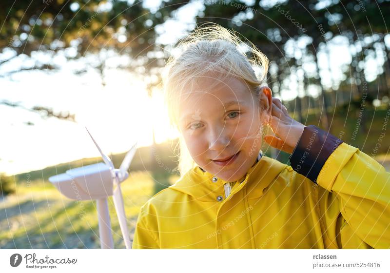 Lächelndes Kind hält Windturbinenmodell bei Sonnenuntergang im Wald und lächelt in die Kamera. Energieerzeugung mit sauberer und erneuerbarer Energie Konzeptbild