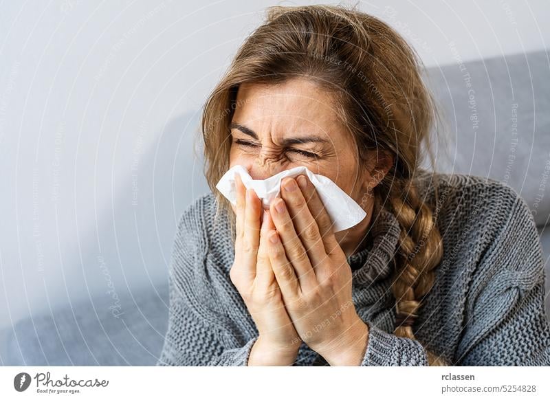 Frau niest in ein Taschentuch im Wohnzimmer. Grippe, Medizin und Gesundheitswesen Konzeptbild Allergie kalt Gewebe Impfstoff Nase sinus Saison Fieber krank