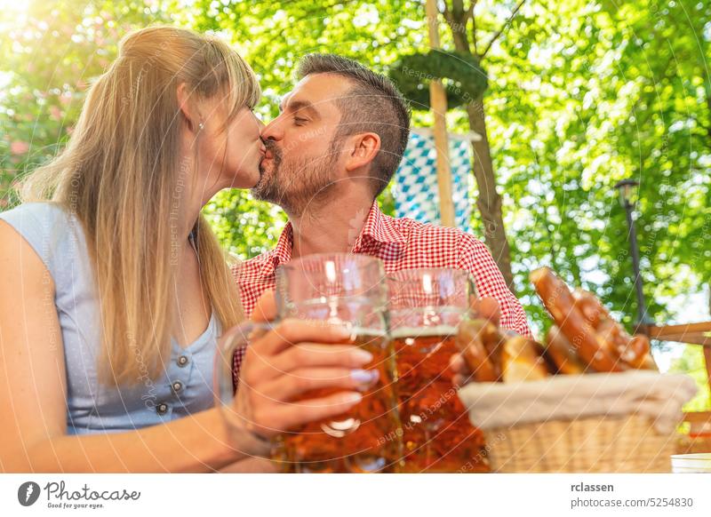 Paar küsst sich und stößt mit einem Krug Bier im bayerischen Biergarten oder auf dem Oktoberfest an romantisch Liebe Kuss Freunde brezen Stadtfest Bayern