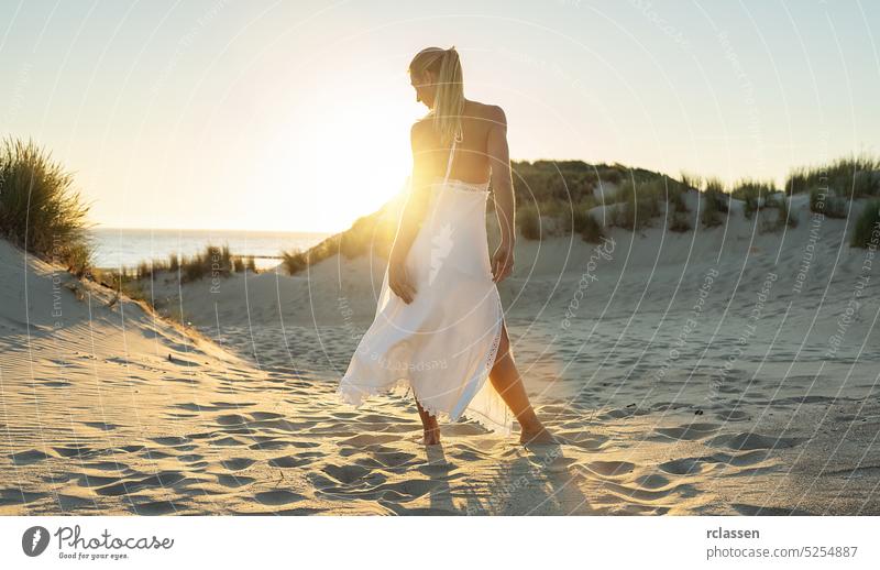 Frau steht barfuß durch Sanddünen in Richtung Meer bei Sonnenuntergang energetisch Hippie Boho Abenteuer allein schön Schönheit wüst Kleid Düne Mode frei