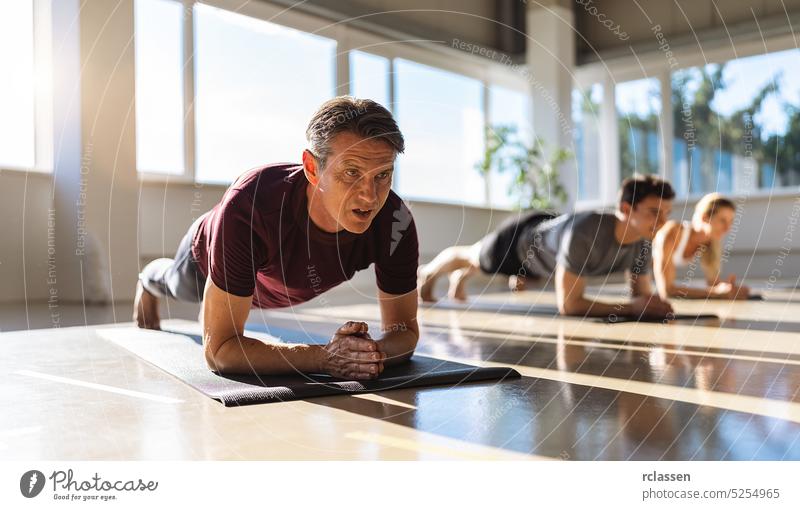 Ein muskulöser Mann und eine Frau machen Planking-Übungen im Fitnessstudio auf einer Yogamatte und stützen sich dabei auf die Ellbogen. Menschengruppe