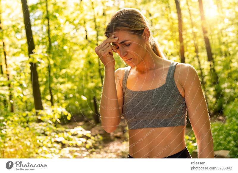 Frau mit Kopfschmerzen beim Training im öffentlichen Park, reibt sich den Kopf Unfall Schmerzen schmerzender Aktivität Athlet sportlich Körpertraining
