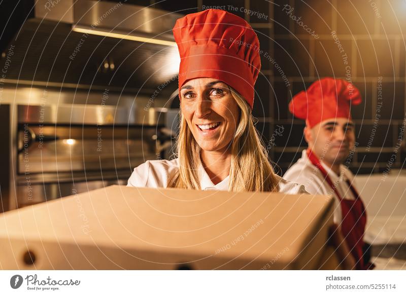 Zufriedenes Pizzabäckerteam, das einem Kunden in einer italienischen Pizzeria frische Pizza in einer Schachtel aus dem Steinofen zur Auslieferung übergibt Team