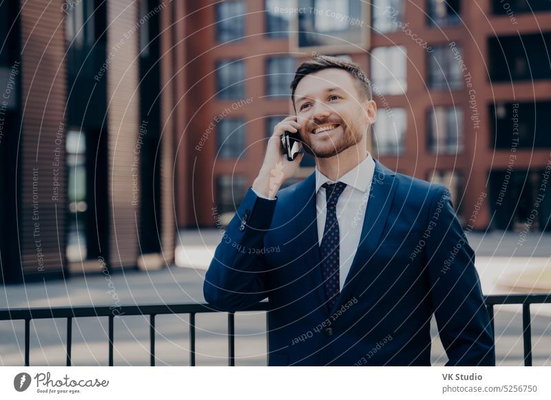 Männlicher Büroangestellter, der ein angenehmes Gespräch am Telefon führt, während er neben einem Bürogebäude im Freien steht gutaussehend Geschäftsmann