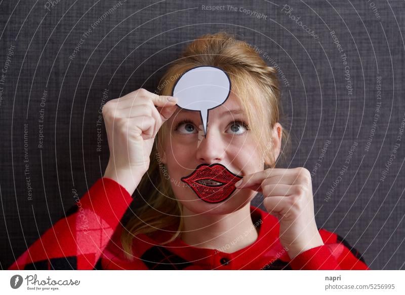 Interpretationsspielraum | Portrait einer jungen Frau, die einen großen roten Mund aus Pailletten und eine leere Sprechblase vor ihr Gesicht hält und dabei einen lustigen Gesichtsausdruck hat.